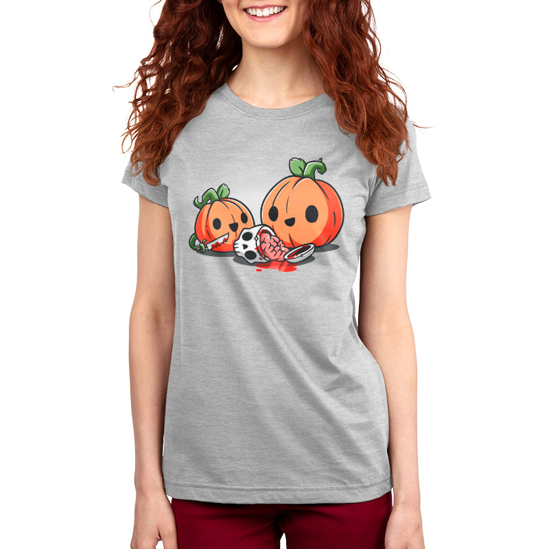 A person in a gray, super soft ringspun cotton t-shirt with a cartoon design of two pumpkins carving another pumpkin and a skeleton head, all smiling. The person is beaming and has long, curly red hair. The t-shirt is called Pumpkin Carving by monsterdigital.