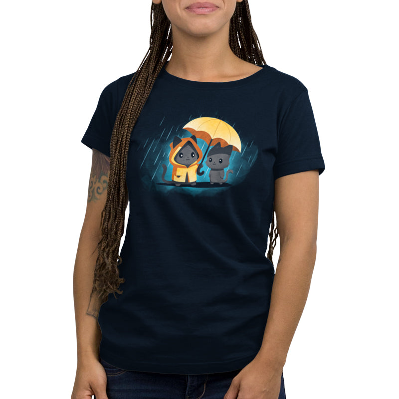A person wearing a navy blue unisex tee with an illustration of two cats, one in a hooded raincoat and the other holding an umbrella. The 100% super soft ringspun cotton fabric ensures maximum comfort. The tee is called Sharing Kindness by monsterdigital.