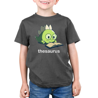 Premium Cotton T-shirt - A child wears a charcoal gray Thesaurus apparel by monsterdigital featuring a cartoon dinosaur reading a book with the word "thesaurus" below the illustration.