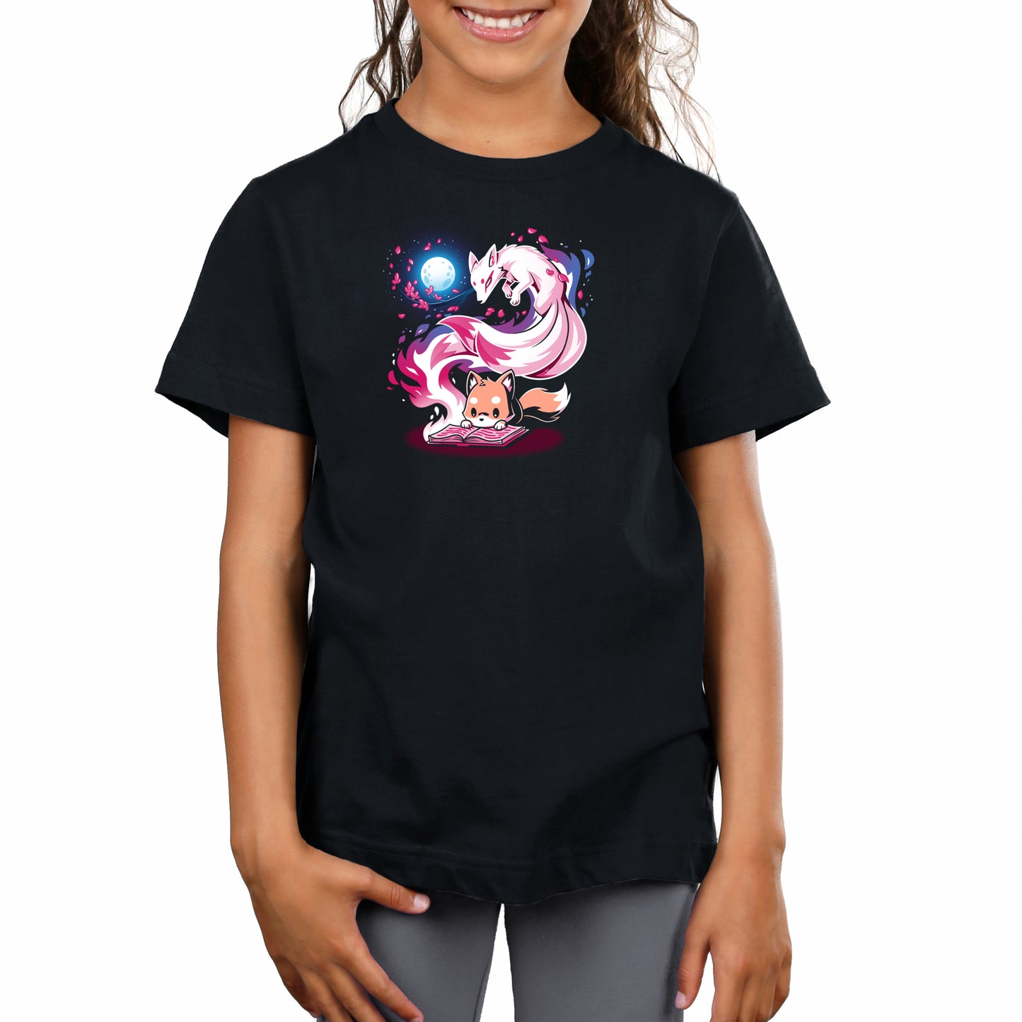 A young girl stands, smiling, wearing a Tale of Tails t-shirt in super soft ringspun cotton by monsterdigital, featuring colorful artwork of two mystical, fox-like creatures beneath a full moon.