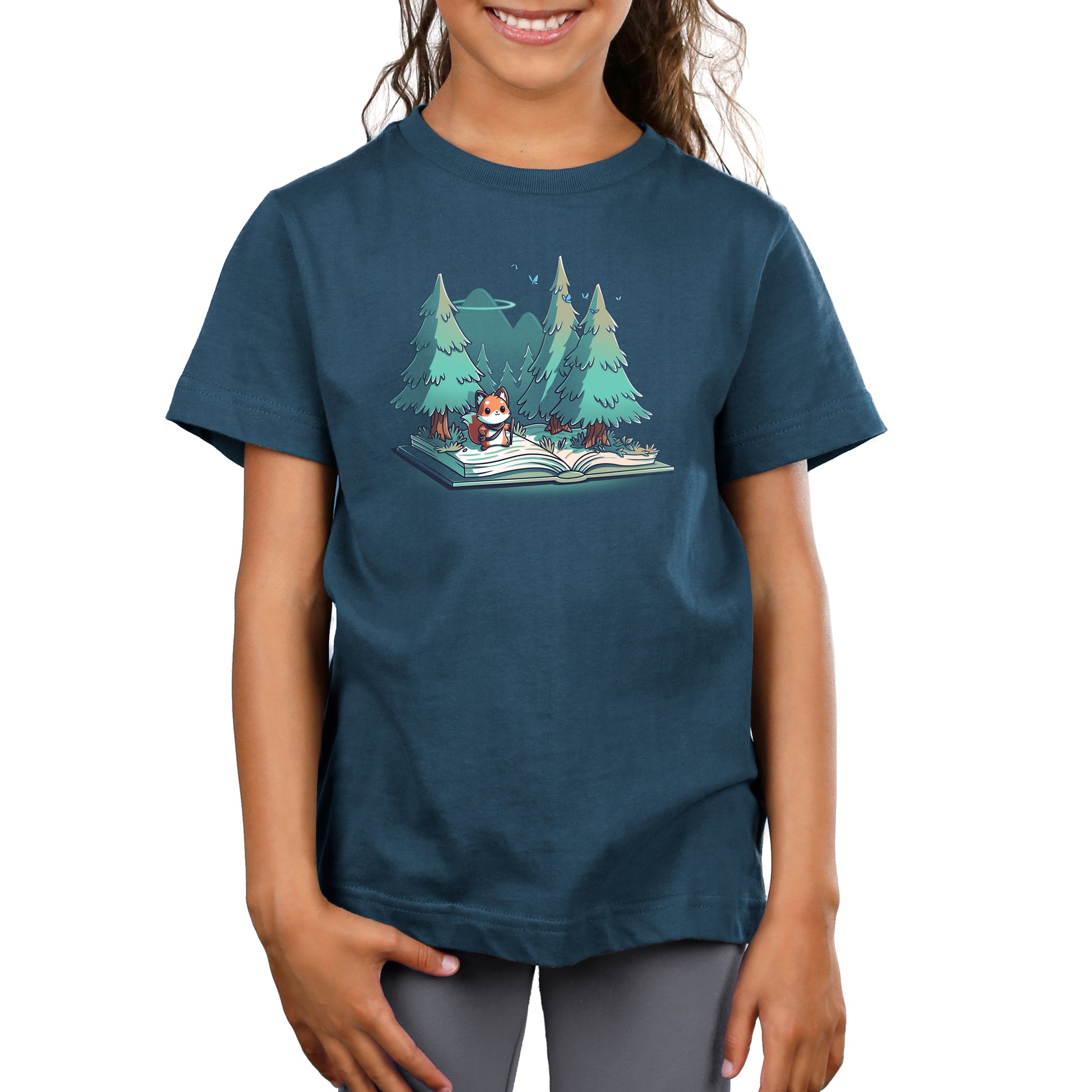 Premium Cotton T-shirt - A young child wearing a denim blue apparel made of super soft ringspun cotton, featuring an illustration of a cat reading "The Adventurer's Tale" in a forest with two trees in the background. The product is named "The Adventurer's Tale" from monsterdigital.