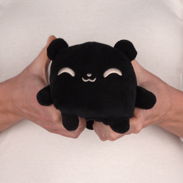 A person holding a TeeTurtle Reversible Bear Plushmate (Black) toy.