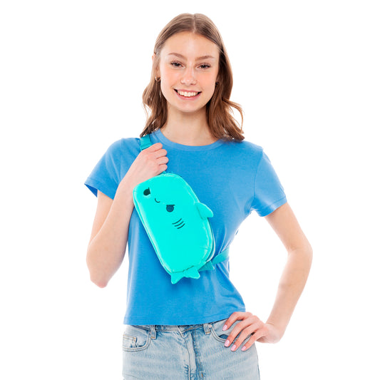A young woman in a blue t-shirt and jeans smiles and holds a TeeTurtle Plushiverse Jaw-some Shark Plushie Fanny Pack.