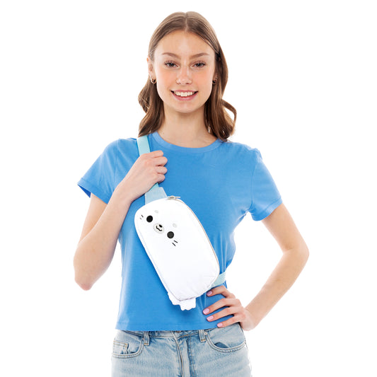 Young woman in a blue t-shirt and jeans, smiling and holding a TeeTurtle Plushiverse Keep it Seal Plushie Fanny Pack, isolated on a white background.