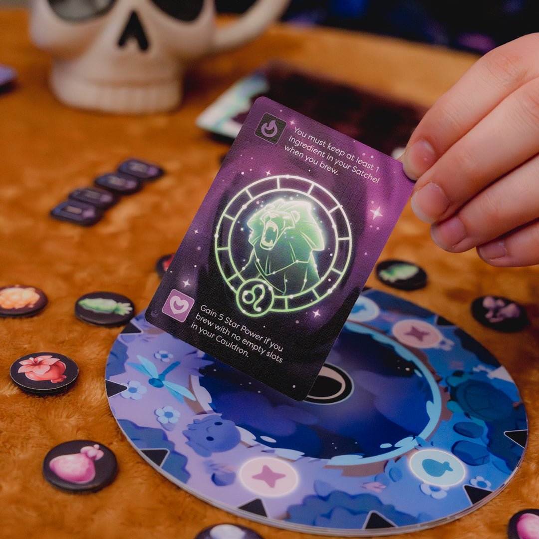 Mystic Moon Curse of the Zodiac Expansion - a hand is holding a card from the expansion above other components