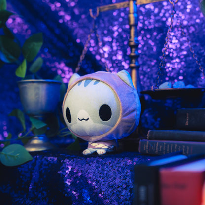 Cloudheads: 5" Mystic Moon (Dex) - A smiling plush gray cat wearing a brown hooded outfit, shown against a sparkly purple background. A plant, scale, and old books are also visible. 