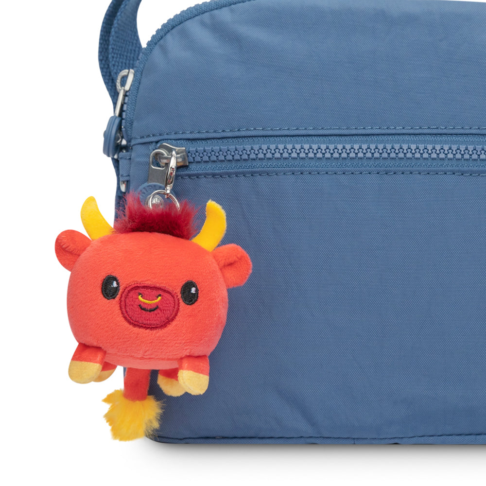 A TeeTurtle Lunar New Year Ox plushie charm keychain is attached to the side of a blue bag as part of a collection.