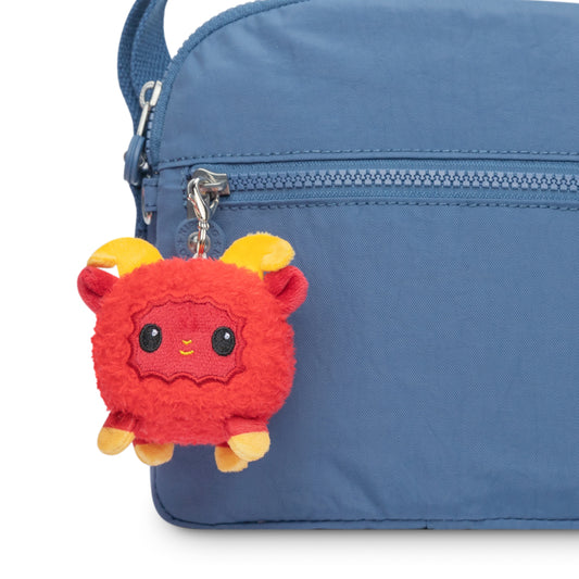 A TeeTurtle Lunar New Year Ram plushie charm keychain is attached to the side of a blue bag, adding a charming addition to your collection.