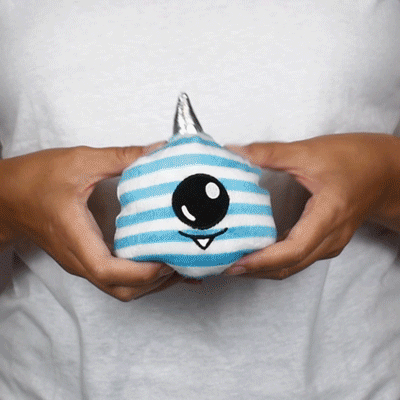A person holding a TeeTurtle Reversible Cyclops Plushie, a blue and white striped stuffed animal.