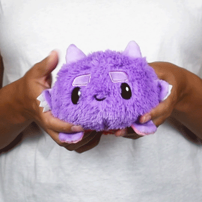 A person holding a TeeTurtle Reversible Fuzzy Monster Plushie.