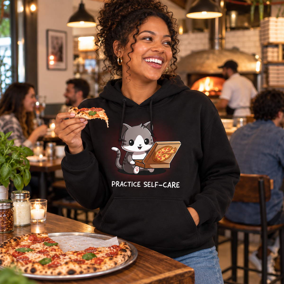 Pullover Hoodie_TeeTurtle black Practice Self-Care Pullover Hoodie featuring a happy gray-and-white cat holding an open pizza box with a pepperoni pizza and the text "Practice Self-Care."