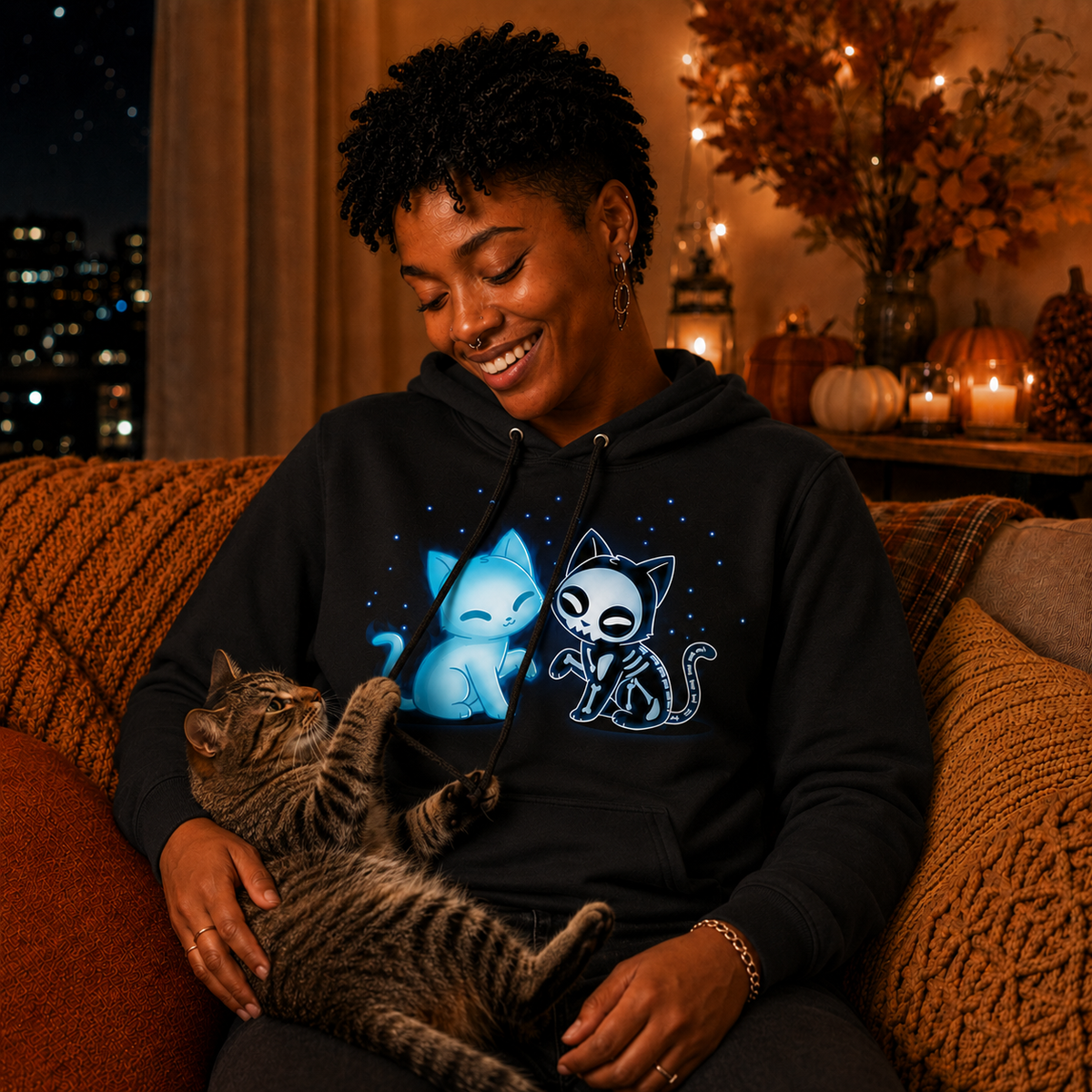 Pullover Hoodie_TeeTurtle black Purranormal Pals Pullover Hoodie featuring a glowing blue ghost cat sitting beside a smiling skeleton cat, surrounded by small blue stars.