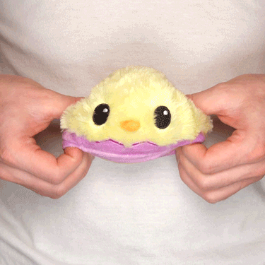 A person holding a TeeTurtle Reversible Chicken & Egg Plushie stuffed toy in yellow and purple.