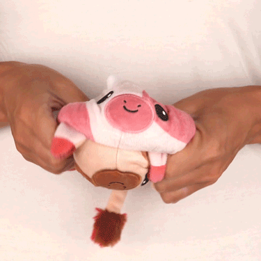 A person holding a pink and white TeeTurtle Reversible Cow Plushie.