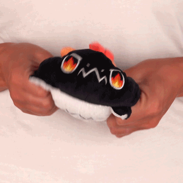 A person holding a TeeTurtle Reversible Dragon Plushie (Black + White Sparkle) with a flame on it, which is a mood plushie.
