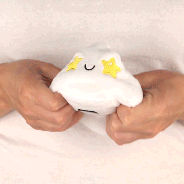 A person holding a TeeTurtle Reversible Ghost Plushie (White Glow) shaped like a white cloud with stars on it.