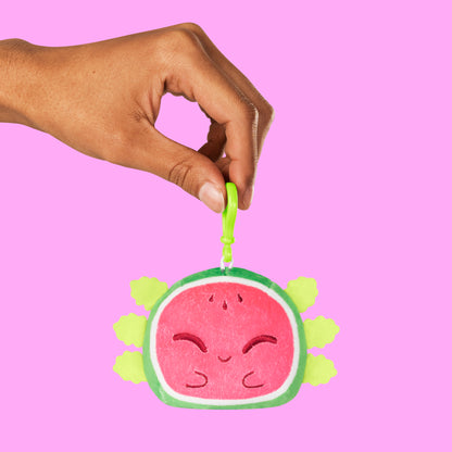 A hand holding a TeeTurtle Plushiverse Alotl Watermelon Reversible Keychain.