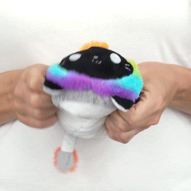 A person holding a TeeTurtle Reversible Lion Plushie (Rainbow Mane) with a rainbow hat.