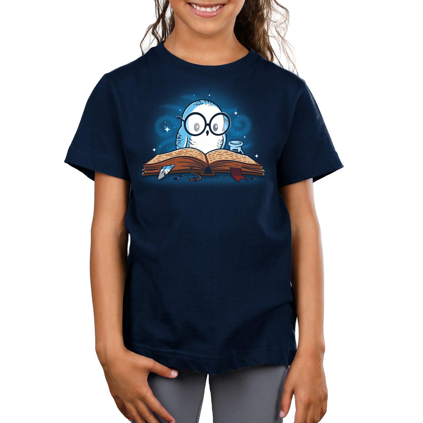 A girl wearing a navy blue TeeTurtle original "Reading is Magical" t-shirt with an image of an owl reading a book.