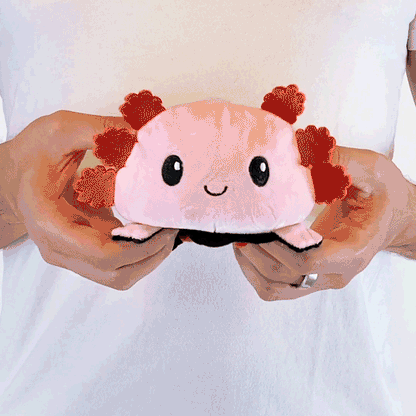 A person holding a TeeTurtle Reversible Axolotl Plushie (Black + Pink) toy.