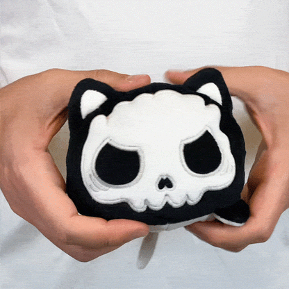 A person holding a TeeTurtle Reversible Cat Plushie (Skeleton Glow) from TeeTurtle.