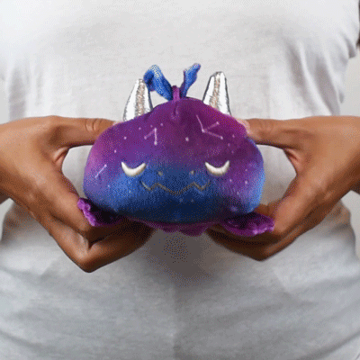 A person holding a TeeTurtle Reversible Dragon Plushie (Purple + Galaxy), featuring purple and blue colors.
