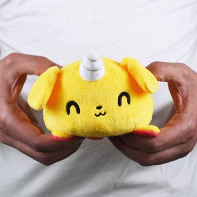 A person holding a TeeTurtle Reversible Puppicorn Plushie (Red + Yellow) stuffed animal.