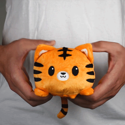 A person lovingly gripping a TeeTurtle Reversible Tiger Plushie stuffed animal.