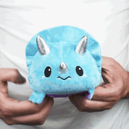 A person holding a TeeTurtle Reversible Triceratops Plushie (Blue + Purple), one of the popular mood plushies from TeeTurtle.