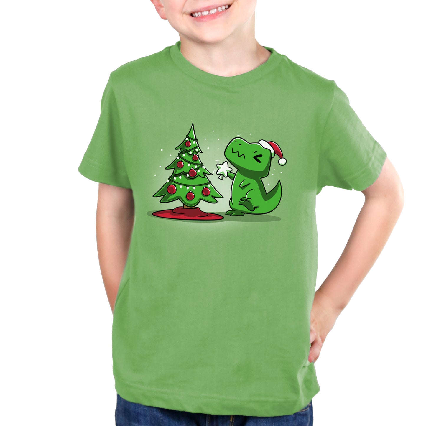 A young boy wearing a TeeTurtle Christmas T-Rex t-shirt next to a Christmas tree.