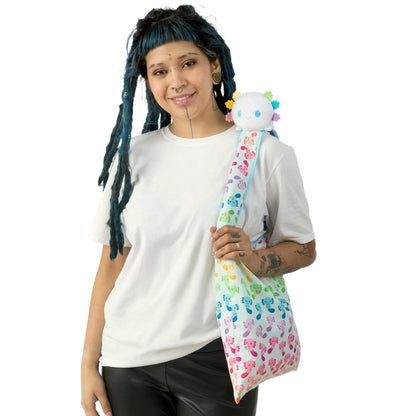 A woman with dreadlocks holding a Plushiverse White Rainbow Axolotl Plushie Tote Bag featuring a Velcro storage pouch made by TeeTurtle.