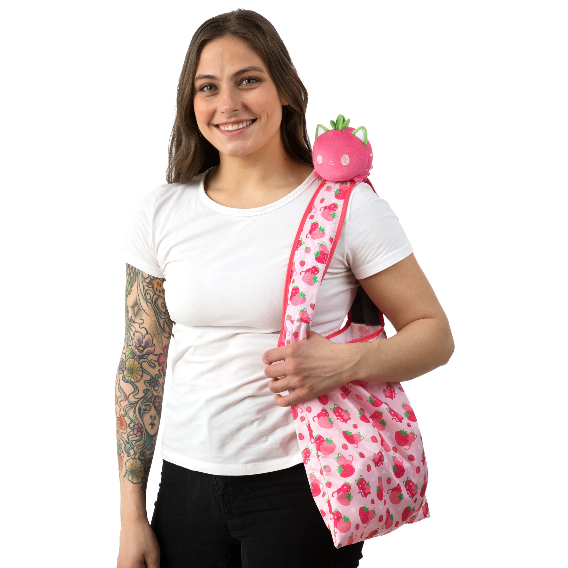 A woman with tattoos holding a TeeTurtle Plushiverse Strawberry Cat Plushie Tote Bag.