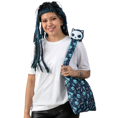 A woman with blue hair and dreadlocks holding a panda stuffed animal, alongside her TeeTurtle Plushiverse Skeleton Cat Plushie Tote Bag.