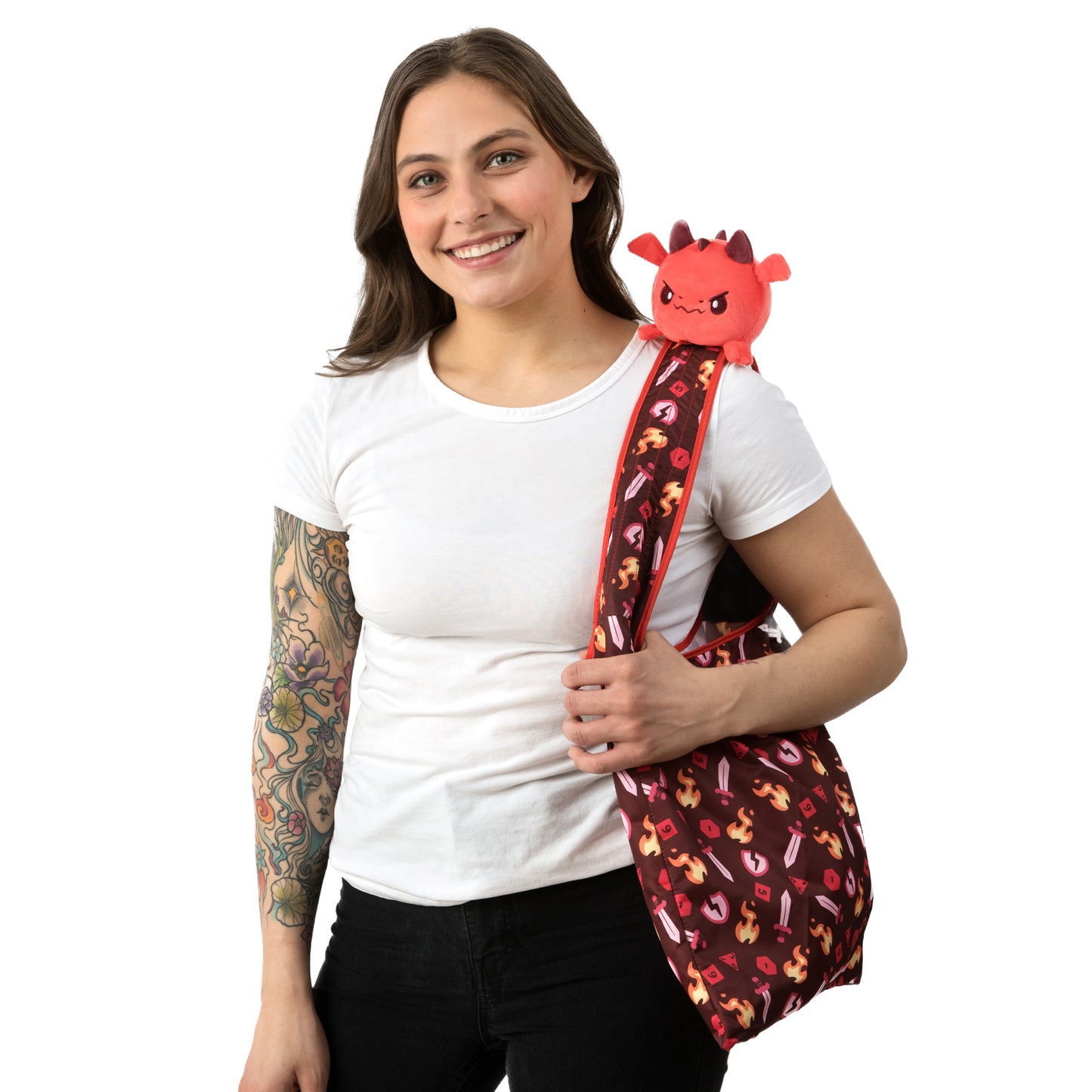 A woman with tattoos holding a Plushiverse Tabletop Dragon Plushie Tote Bag from TeeTurtle.