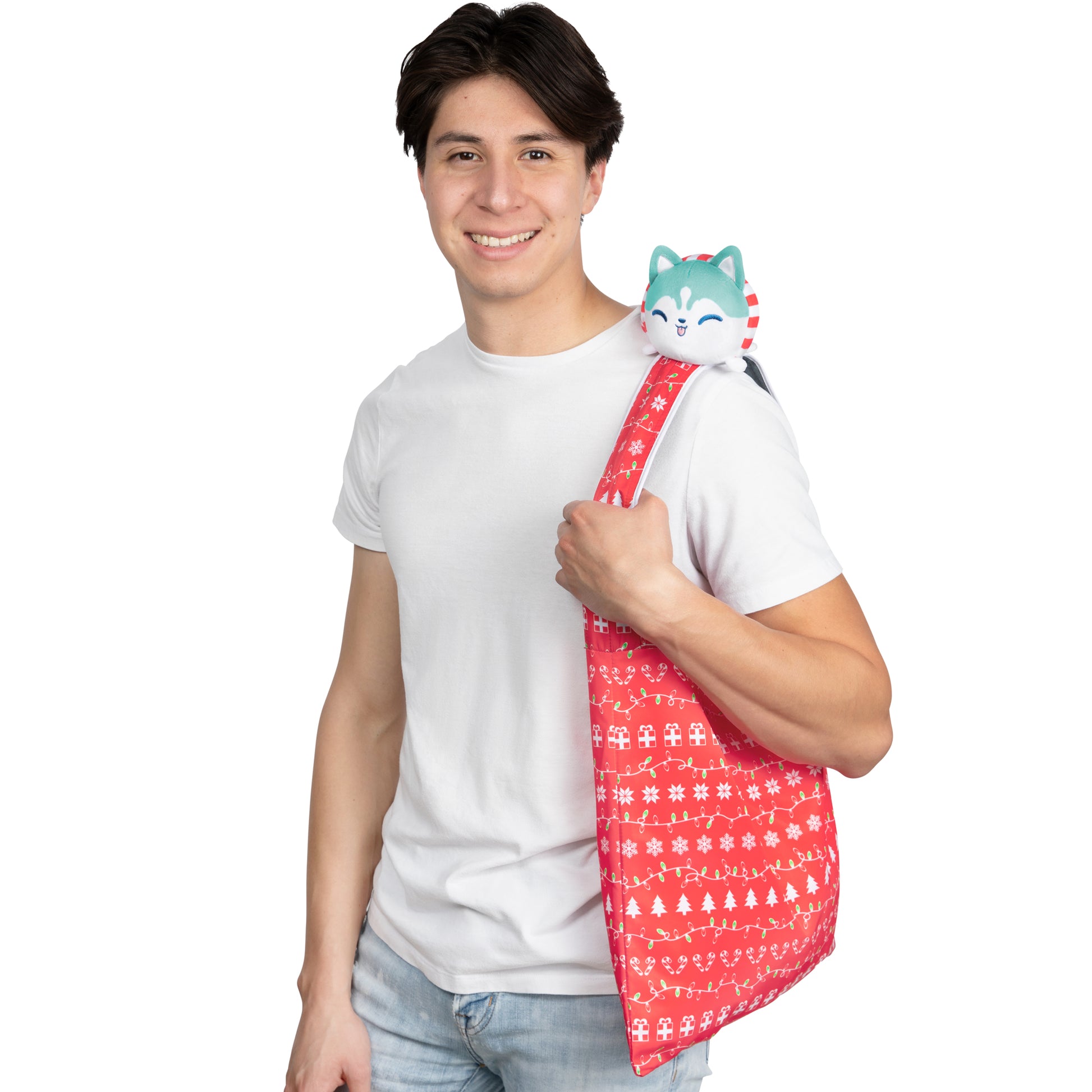 A young man holding a TeeTurtle Plushiverse Holiday Husky Plushie Tote Bag in a velcro storage pouch.