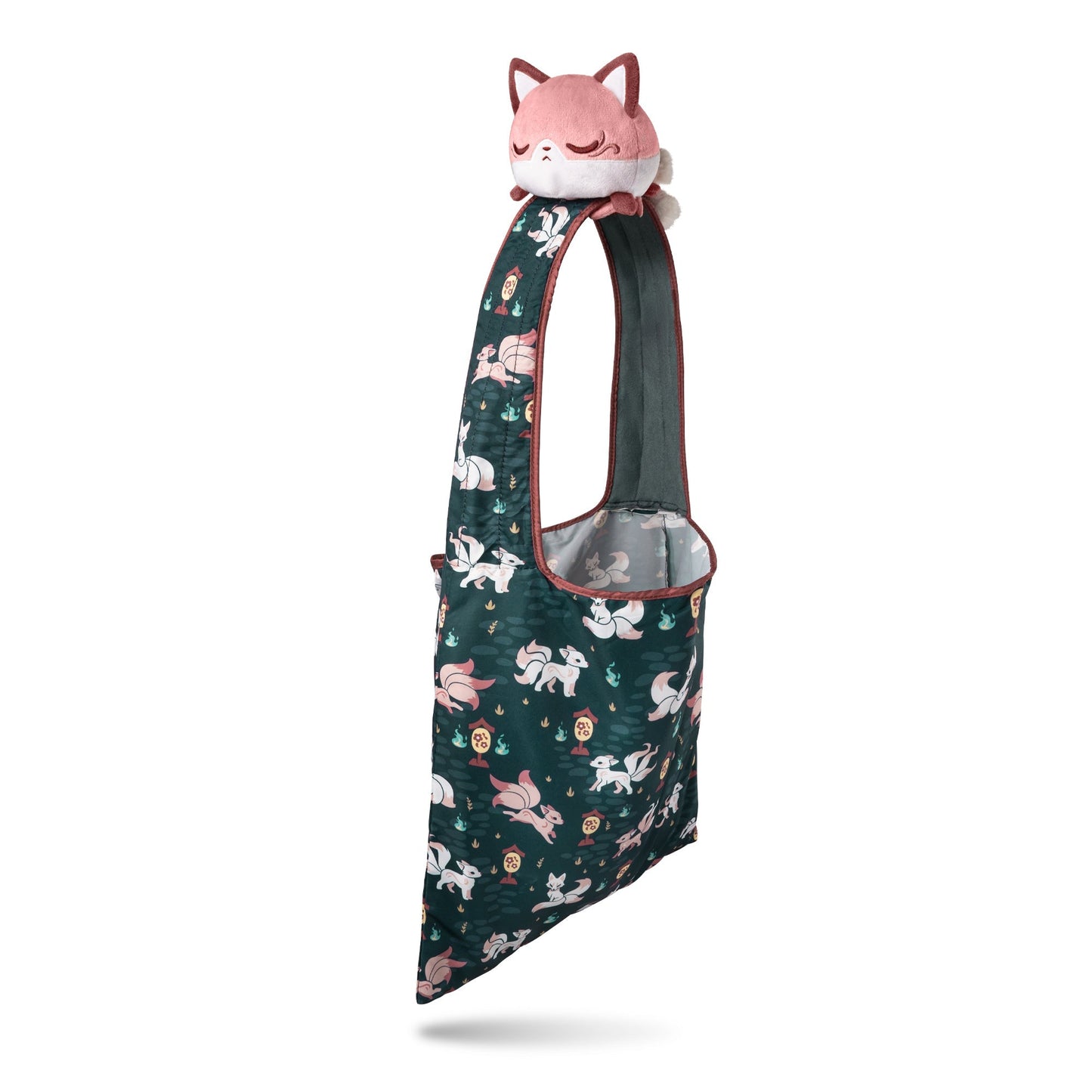 A green recycled Plushiverse Enchanting Kitsune Tote Bag with a pink TeeTurtle plushie on top, featuring an intricate pattern of plants and animals in a whimsical design, isolated on a white background.