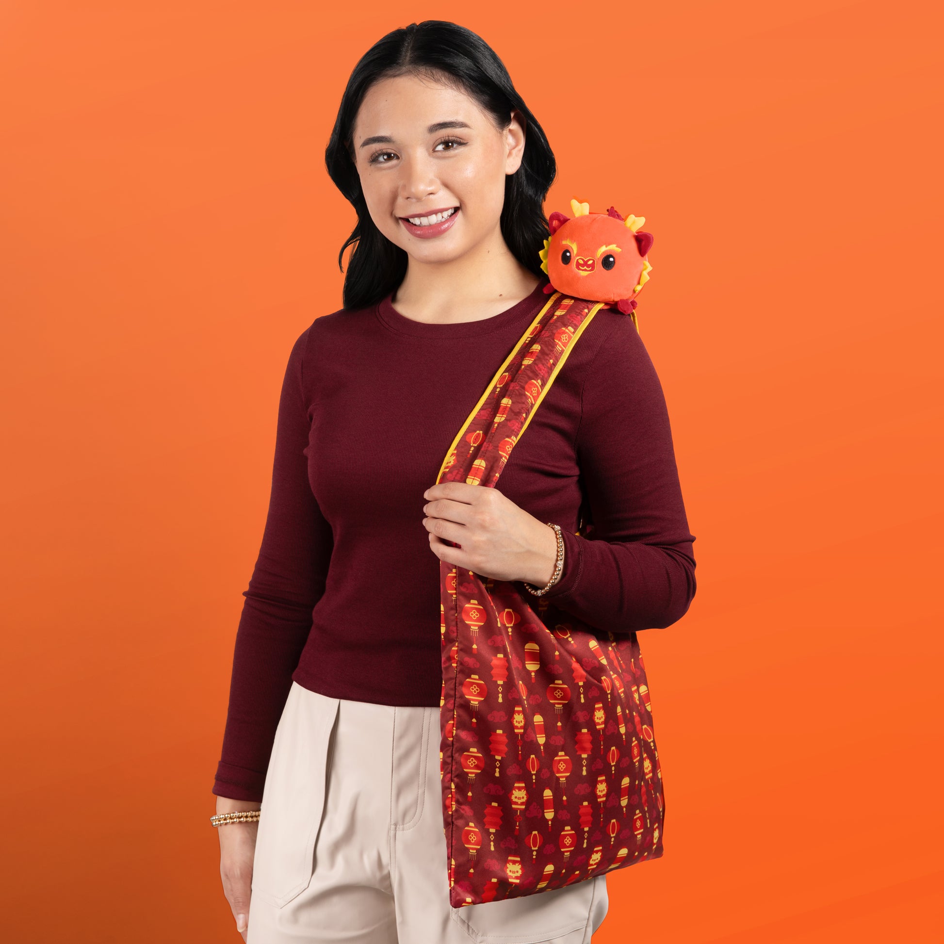 A woman holding a TeeTurtle Plushiverse Lunar New Year Dragon Plushie Tote Bag with a teddy bear in it, perfect for Lunar New Year celebrations.