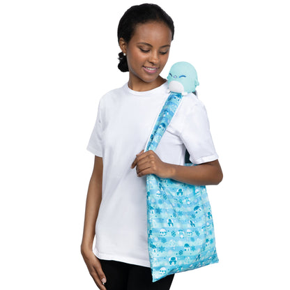 A woman carrying a Plushiverse Snowy Penguin Plushie Tote Bag embellished with a blue stuffed animal from TeeTurtle.