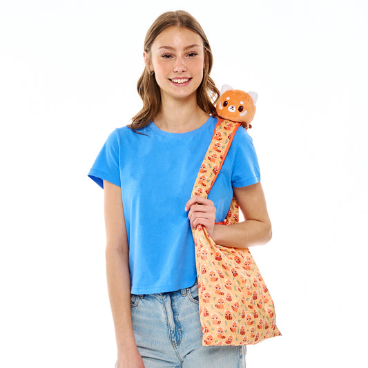 Young woman in a blue t-shirt and jeans holding a TeeTurtle Plushiverse Bamboo Snack Plushie Tote Bag with a cute animal design.