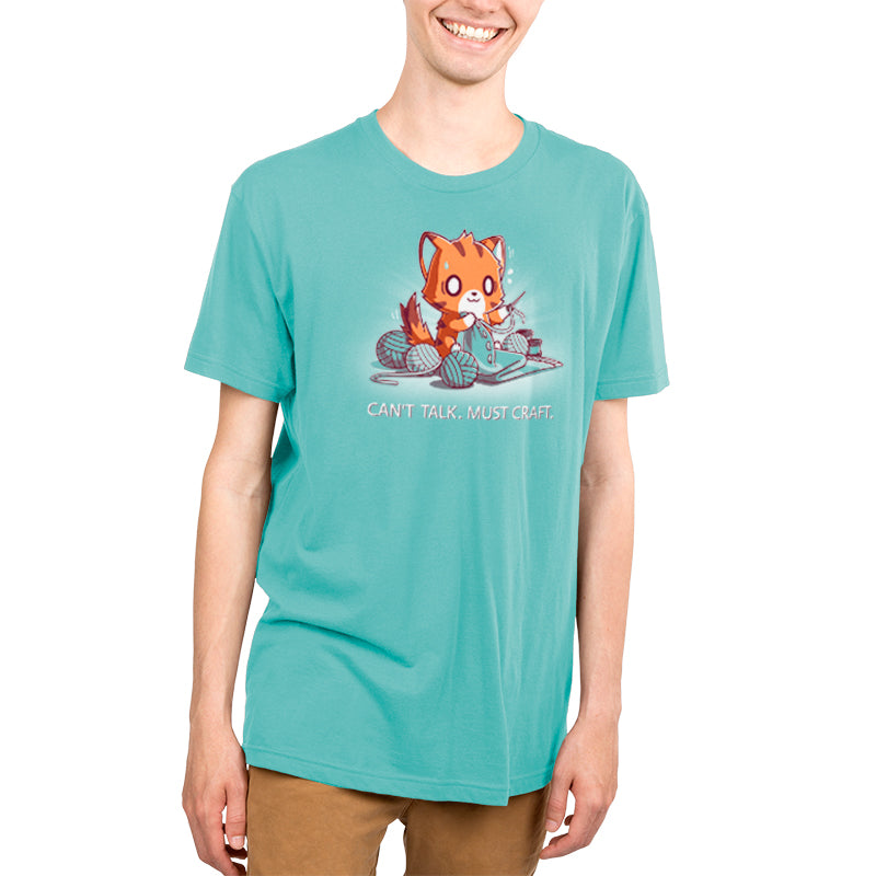 A person wearing a Caribbean blue t-shirt with a cartoon of a fox knitting and the text "Can't Talk. Must Craft," made from super soft ringspun cotton for ultimate comfort by monsterdigital.