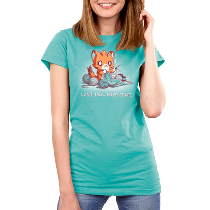 A person wearing a Caribbean blue t-shirt featuring a cartoon fox knitting and text that reads, "Can’t Talk. Must Craft" by monsterdigital. The super soft ringspun cotton tee complements their smile as they touch their hair.