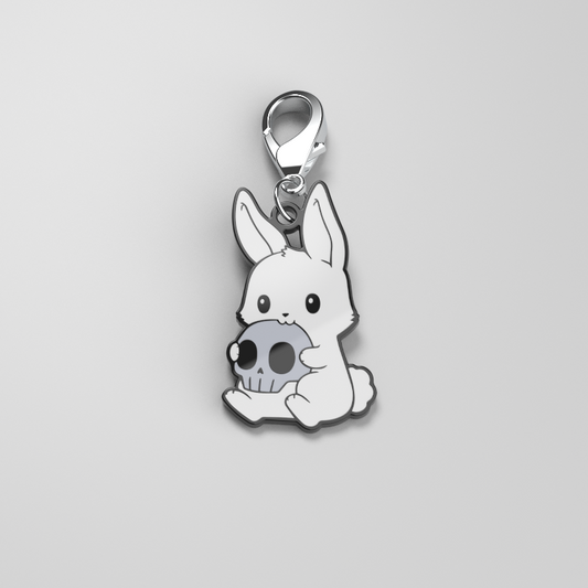 A white bunny wearing an Adorable Monstrosity Enamel Keychain with a skull charm and attached to a metal clip. (Brand: TeeTurtle)