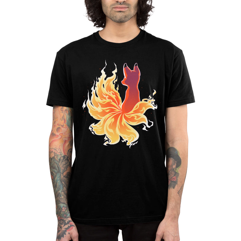A person wearing a black unisex tee by monsterdigital with a design of a Fire Kitsune, featuring a flaming fox with multiple tails. The super soft ringspun cotton fabric complements their long hair and the tattoos on their arms.
