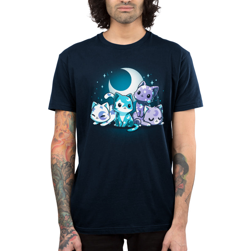 A person with tattoos on their arms is wearing a super soft ringspun cotton navy blue Moon & Star Meows t-shirt by monsterdigital featuring an illustration of four colorful, cartoon-style cats under a crescent moon, perfect for stargazing companions.