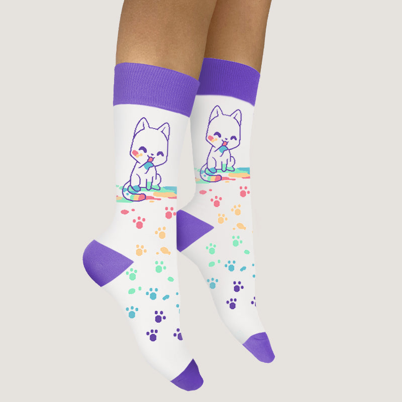 A woman wearing TeeTurtle Rainbow Paw Print Socks with a white cat and paw prints.