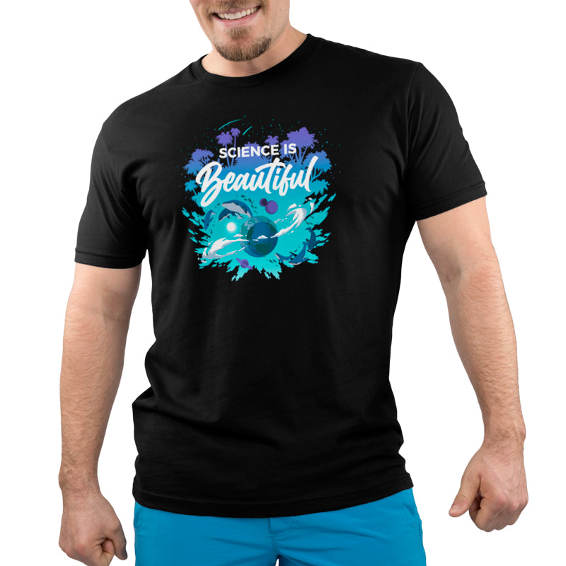 A person is wearing a super soft ringspun cotton black T-shirt from monsterdigital that proudly displays the phrase "Science is Beautiful" along with an artistic illustration related to science on the front. They are also wearing bright blue pants and smiling.