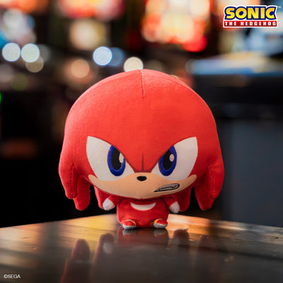 Knuckles Cloudhead plushie with Mom's Choice Award seal. He has a big head, tiny body and a determined expression on his face. He is sitting on a wood table with blurry arcade machines behind him. 