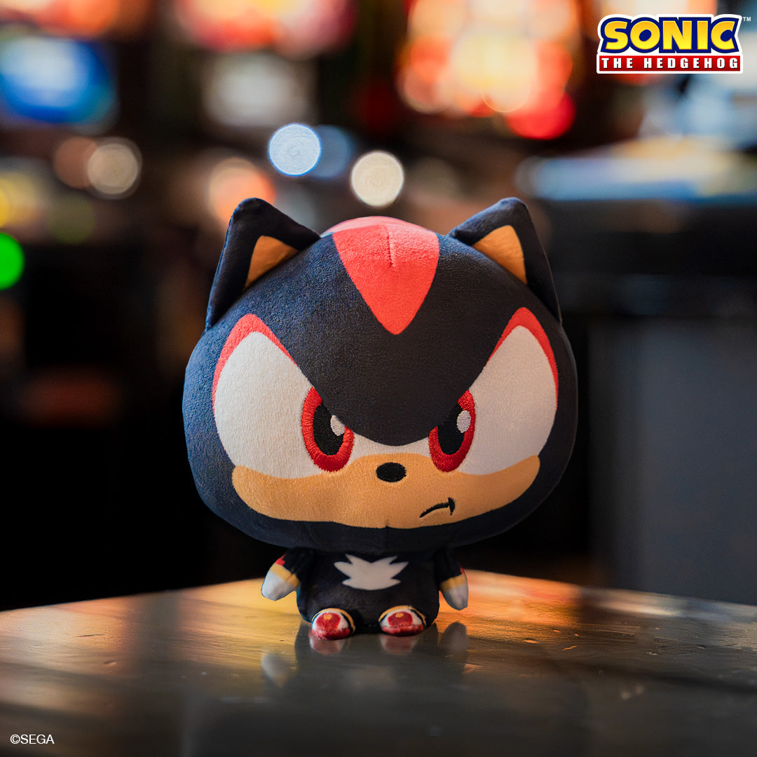 Shadow Cloudhead with a Mom's Choice Awards seal in the upper left corner. He has a big head, tiny body and is frowning. He is sitting on a wood table with a blurry arcade behind him. 