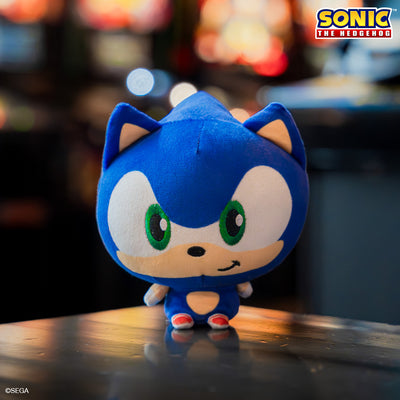 Sonic the Hedgehog Cloudhead - this plushie has a big head, tiny body, and is smirking. He is sitting on a table with blurry lights behind him. 