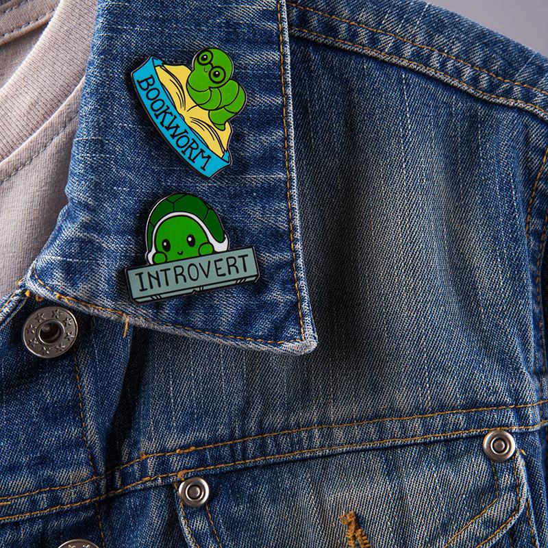 A denim jacket adorned with two TeeTurtle Bookworm Pins.